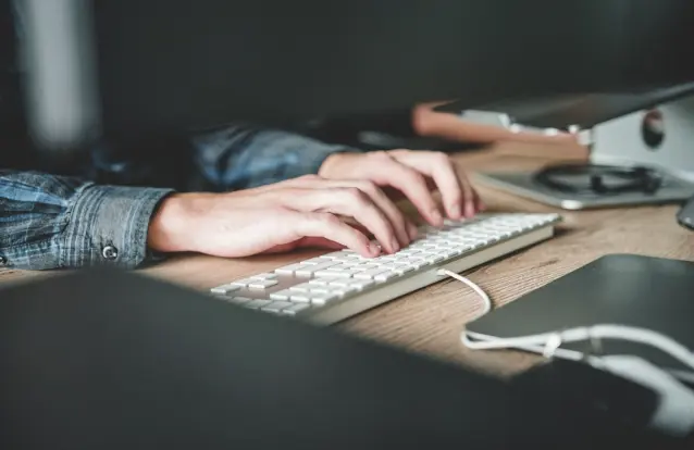 A person focused on typing at a desk, illustrating the use of self-service knowledge base software.